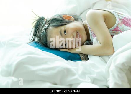 Liebenswert asiatische kleine Mädchen erwachte in ihrem Bett und Blick auf Kamera. Stockfoto