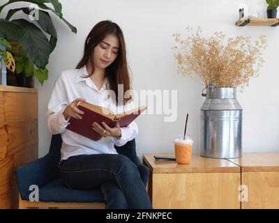 Portrait eines weiblichen Teenagers, der ein Buch liest, während er darauf sitzt Sessel im Wohnzimmer Stockfoto