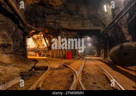 Tunnel des Bergbaus einer unterirdischen Mine. Viele Rohrleitungen an der Decke und Schienenbahn für Trolleys Stockfoto