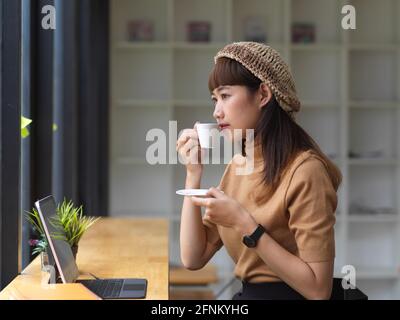 Seitenansicht eines weiblichen Teenagers, während er sich beim Kaffeetrinken entspannt Arbeiten mit Tablet im Café Stockfoto