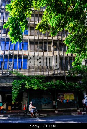 Am späten Nachmittag radelt ein Mann in der Chinatown-Gegend von Bangkok, Thailand, an einem alten grauen Gebäude vorbei Stockfoto