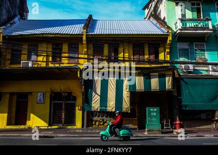 Ein Mann auf einem alten grünen Vespa-Roller fährt an einer restaurierten, gelb gefärbten Ladenfront in der Chinatown-Gegend von Bangkok, Thailand vorbei Stockfoto