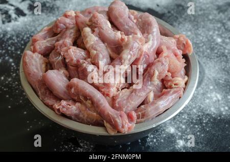 Rohe Hühnerhälse in einer Metallschüssel auf schwarzem Hintergrund. Eine volle Schüssel mit Hühnerfleisch aus Edelstahl. Essen, Zutaten. In Innenräumen. Stockfoto