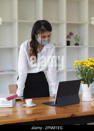 Porträt einer jungen schönen Studentin, die Maske trägt und in der Bibliothek arbeitet Stockfoto