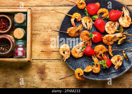 Leckere gegrillte Garnelen auf Holzspießen mit Erdbeeren. Geröstete Garnelen, Meeresfrüchte Stockfoto