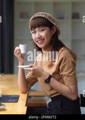 Junge hübsche asiatische Frau hält eine Tasse Kaffee, während Blick auf die Kamera Stockfoto