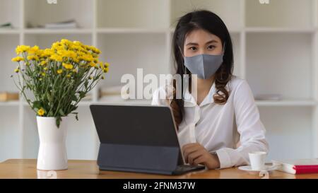 Junge Geschäftsfrau trägt Gesichtsmaske, die im Büro arbeitet Zimmer Stockfoto
