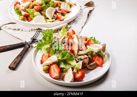 Leckerer Salat mit Jamon, Erdbeeren, Trauben, Mozzarella und Oliven mit Granatapfelsauce. Gesunde und ausgewogene Ernährung. Bio-Lebensmittel Stockfoto