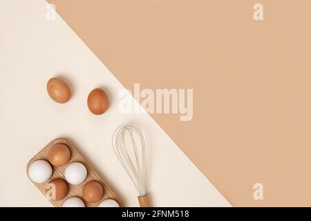 Eier in Holzeischachtel und Schneebesen auf beigem Hintergrund. Flach liegend Draufsicht Kopierbereich. Stockfoto