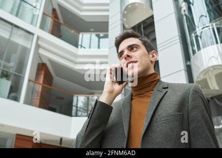 Junge Architektin, die mit dem Mobiltelefon spricht, während sie im Freien steht Modernes Bürogebäude im Hintergrund Stockfoto