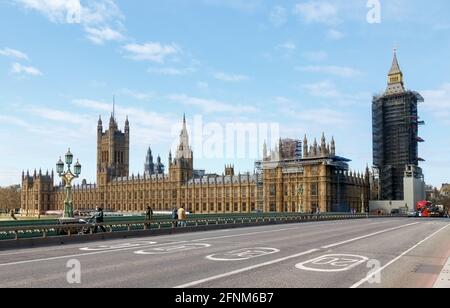 Die Häuser des Parlaments von der Westminster Bridge mit Menschen, die Gesichtsmasken tragen, sind sozial voneinander entfernt und Fahrzeuge am Ende der Brücke. Stockfoto