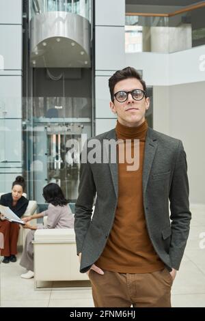 Porträt eines jungen Geschäftsmannes in einer Brille, der die Kamera anschaut Im Büro mit seinen Kollegen im Hintergrund Stockfoto