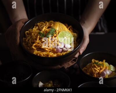 Ein kurzer Schuss von Hand hält eine Schüssel mit Noodles-Kurrsuppe mit Huhn (Khao Soi), nordthailändischer Küche Stockfoto