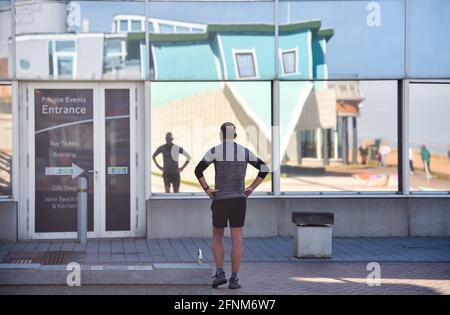 Brighton UK 18. Mai 2021 - EIN Läufer spiegelt sich an einem schönen, warmen, sonnigen Morgen in den Brighton i360-Fenstern in der Nähe des Upside Down House wider, aber für den späteren Tag in ganz Großbritannien wird ein unruhiger Wetterbericht prognostiziert : Credit Simon Dack / Alamy Live News Stockfoto