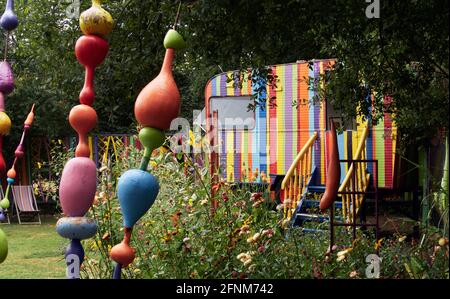 Corps-Nuds, Frankreich. Ille-et-Vilaine Abteilung.. Der bunte Garten bringt einen alten Wohnwagen zusammen, der mit Farblinien bemalt ist, umgeben von sehr c Stockfoto