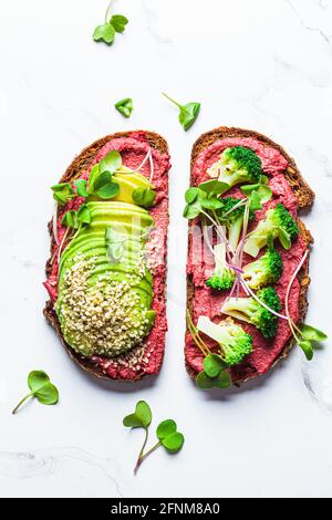 Toasts mit Beetroot-Hummus, Avocado und Brokkoli, weißer Marmorhintergrund, Draufsicht. Veganes Lebensmittelkonzept. Stockfoto