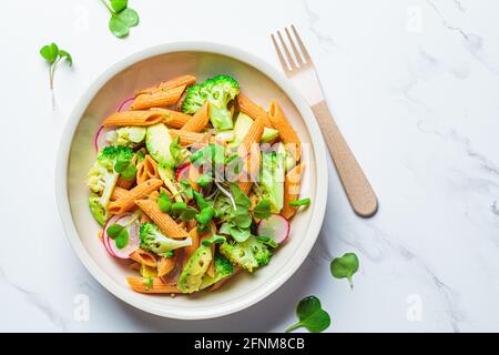 Linsen-Pasta mit Brokkoli, Avocado, Rettich und Sprossen in einer weißen Schüssel. Gesundes veganes Rezeptkonzept. Stockfoto