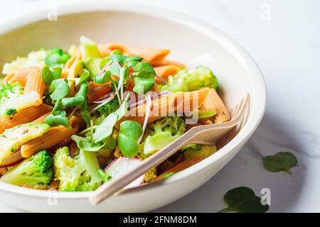 Linsen-Pasta mit Brokkoli, Avocado, Rettich und Sprossen in einer weißen Schüssel. Gesundes veganes Rezeptkonzept. Stockfoto