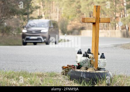 Ein Gedenkkreuz am Straßenrand mit Kerzen zum Gedenken an den tragischen Tod, auf einer Fahrt im Hintergrund verschwommenes Auto. Stockfoto