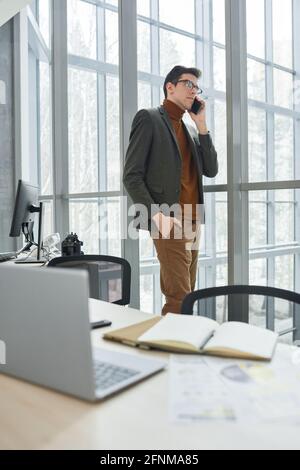 Junger Geschäftsmann, der während der Arbeit bei Modern mit dem Mobiltelefon spricht Büro Stockfoto