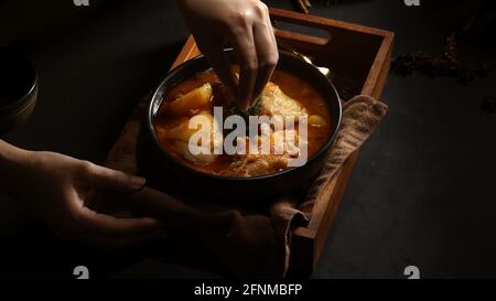 Zugeschnittenes Bild des weiblichen Hähnchens, das von Hand zubereitet wird, Massaman Curry To Serviert im thailändischen Restaurant Stockfoto