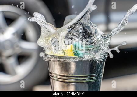 Ein Schwamm fällt mit einem Spritzer Waschmittel in den Eimer. Händewasch mit Seifenwasser. Stockfoto