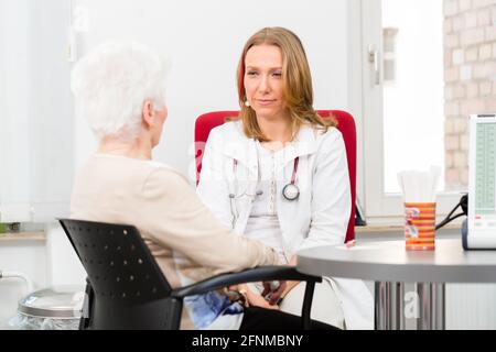 Junge Ärztin mit Rentner in Chirurgie Sprechstunde am Schreibtisch saß Stockfoto