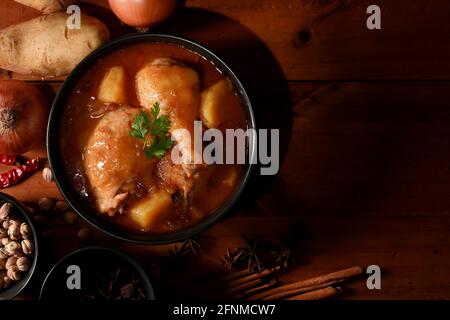 Blick von oben auf die Massaman Curry-Suppe mit Zutaten auf dem Holztisch, traditionelles thailändisches Essen Stockfoto