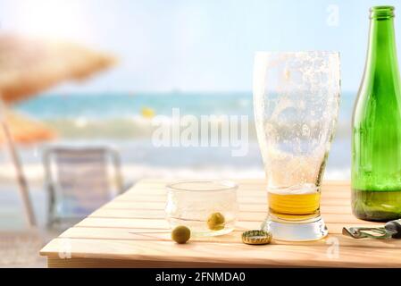 Aperitif am Strand mit einem Glas Bier Und eine Schüssel mit fast leeren Oliven Stockfoto