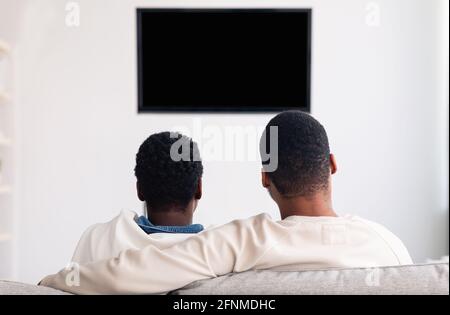 Schwarzes Paar, das mit Mockup Fernsehen schaut und auf dem Sofa sitzt Stockfoto