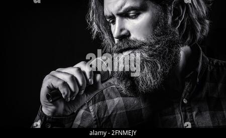 Männer nehmen an Karaoke Teil. Mann mit einem Bart, der ein Mikrofon hält und singt. Mann, der mit Mikrofon singt. Männlicher Gesang mit Mikrofonen. Bärtiger Mann Stockfoto