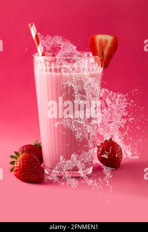 Erdbeer-Milchshake spritzt in Glas auf rosa Hintergrund Stockfoto