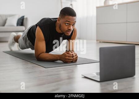 African Guy Tun Elbow Plank Übung Auf Laptop Zu Hause Stockfoto