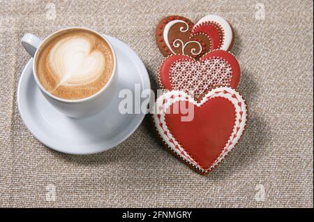 Morgenliebe. Tasse Kaffee und drei herzförmige Kekse mit Glasur Draufsicht Stockfoto