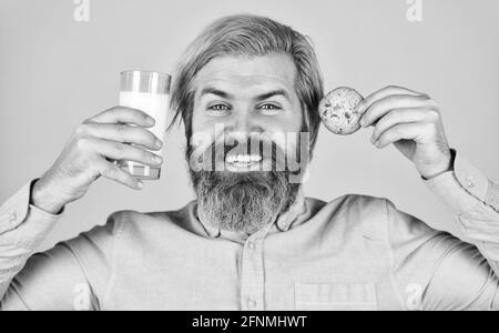 Bärtiger Mann trinkt Milch mit Keksen. Lassen Sie es für den Weihnachtsmann. Frühstück oder Mittagessen. Milch und süße Kekse. Happy Hipster Eat Cookie Dessert. Köstlich Stockfoto