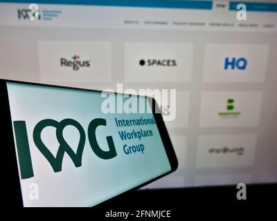 Mobiltelefon mit Logo des multinationalen Serviced Offices-Unternehmens IWG plc auf dem Bildschirm vor der Webseite. Konzentrieren Sie sich auf die Mitte links des Handydisplays. Stockfoto