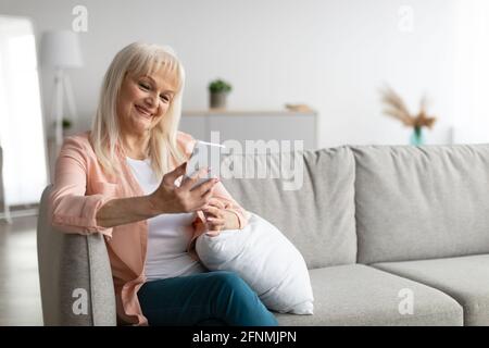 Lächelnde reife Frau mit Smartphone auf der Couch sitzen Stockfoto