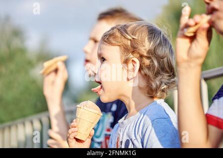 Entzückender kleiner Junge mit älteren Brüdern isst leckeres Schokoladeneis Creme sitzt zusammen auf verschwommenem Hintergrund in Park Nahaufnahme Stockfoto