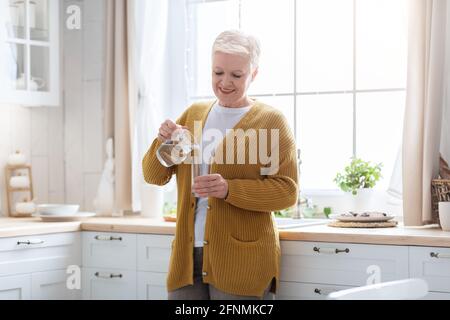 Fröhliche Großmutter, die in der Küche steht und Wasser in das Glas gießt Stockfoto