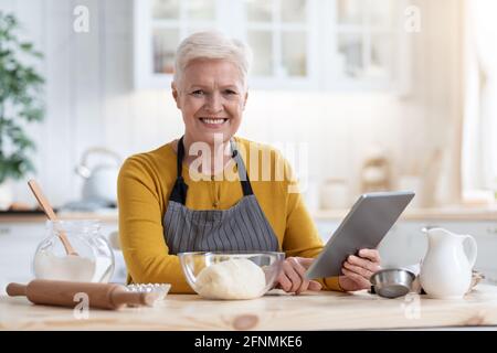 Glückliche alte Frau Kochen nach Rezepten aus dem Internet Stockfoto