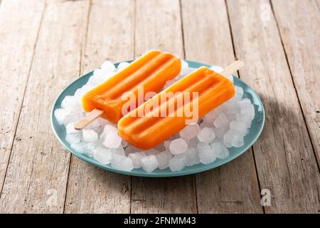 Orangefarbene Eiszapfen auf blauem Teller auf Holztisch Stockfoto
