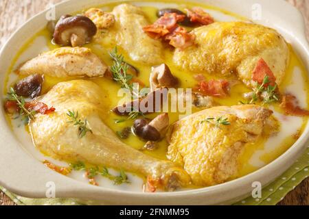 Geschmortes Huhn in Weißwein mit Rahm, Speck und Pilzen in Nahaufnahme in einem Topf auf dem Tisch. Horizontal Stockfoto