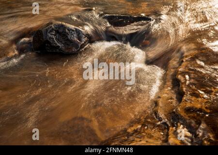 Das Sonnenlicht reflektiert sich von einer kleinen Kaskade auf dem Burn Anne Water in der Nähe von Galston in East Ayrshire, Schottland. Stockfoto