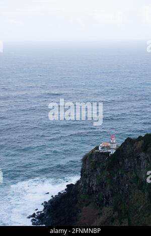 Ein Leuchtturm in der Nähe von Nordese auf den Azoren, Portugal. Der Horizont blickt nach Westen in den Atlantischen Ozean und der Leuchtturm steht als einziger Farbtupfer. Stockfoto