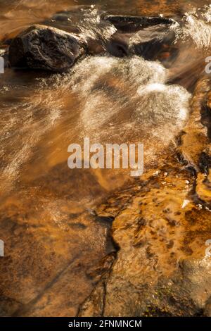 Das Sonnenlicht reflektiert sich von einer kleinen Kaskade auf dem Burn Anne Water in der Nähe von Galston in East Ayrshire, Schottland. Stockfoto