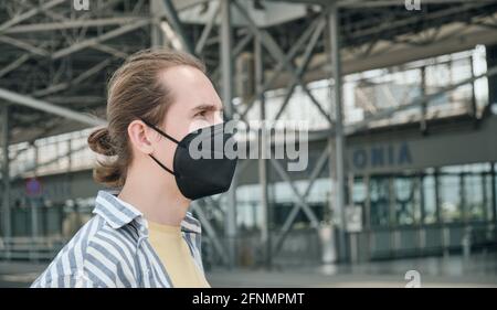 Junger Tourist, der im Flughafen eine schwarze, wiederverwendbare Gesichtsmaske trägt. Stockfoto