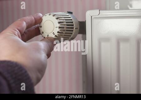 Hand schaltet den Heizkörper Thermostat auf ein Minimum mit der Ankunft des Frühlings und Erwärmung in der Wohnung gegen. Stockfoto