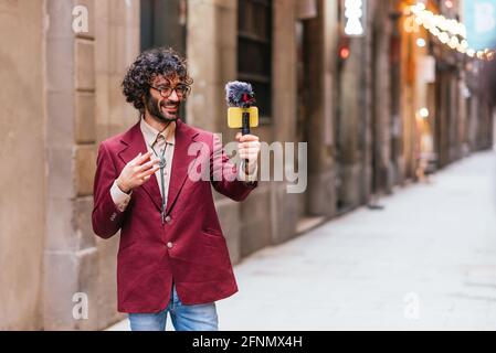 Attraktiver Kaukasischer, der sich in den Straßen von Barcelona aufnahm. Er hält einen Gimbal mit einem gelben Handy und einem Mikrofon. Er ist dres Stockfoto