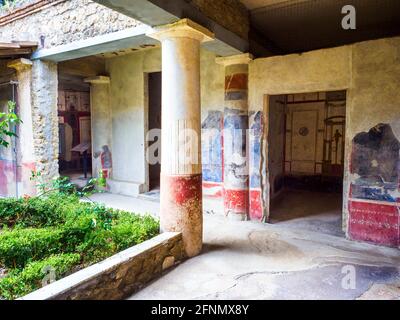 Kleine Peristylsäulen, die unten rot gestrichelt und oben weiß gestrichen sind. Eine niedrige Mauer trennt die Kolonnade vom kleinen zentralen Garten. Die Wände des Peristyls sind im vierten Stil mit schwarzen Paneelen verziert, die durch architektonische Motive über einem unteren roten Fries getrennt sind - Haus des Octavius Quartio - archäologische Stätte von Pompeji, Italien Stockfoto