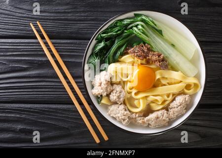 Köstliche asiatische hausgemachte Nudelsuppe mit gebratenen Sardellen, Fleischbällchen und Bok Choy aus nächster Nähe in einer Schüssel auf dem Tisch. Horizontale Draufsicht von oben Stockfoto